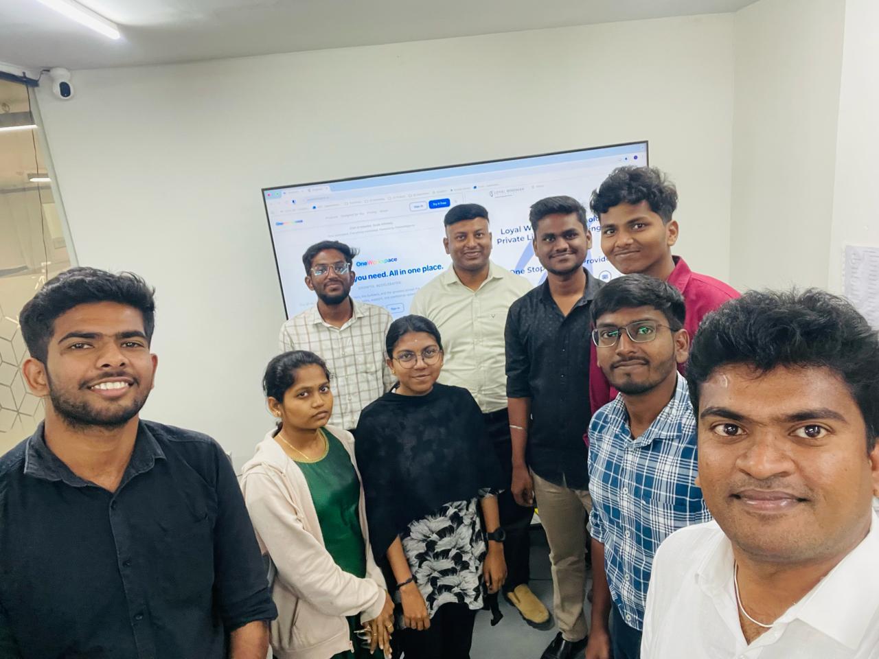 Jagadeeshwaran taking a selfie with the Loyal Wingman Technologies team on launch day, with our website on the screen behind them.